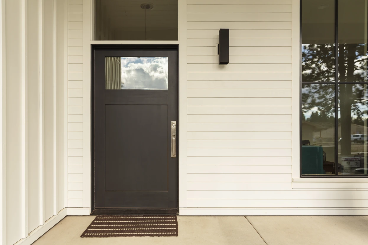 Entrée extérieure de maison moderne avec porte d'entrée contemporaine noire à panneau vitré supérieur et poignée métallique dorée