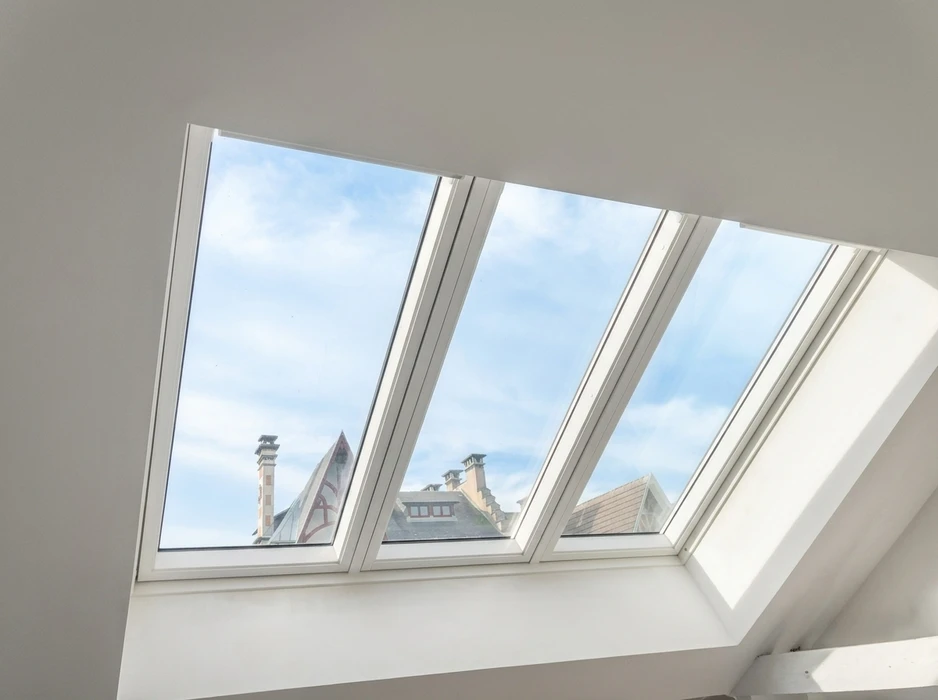 Intérieur lumineux avec triple fenêtre de toit en pente, cadres blancs en PVC, vitrage clair