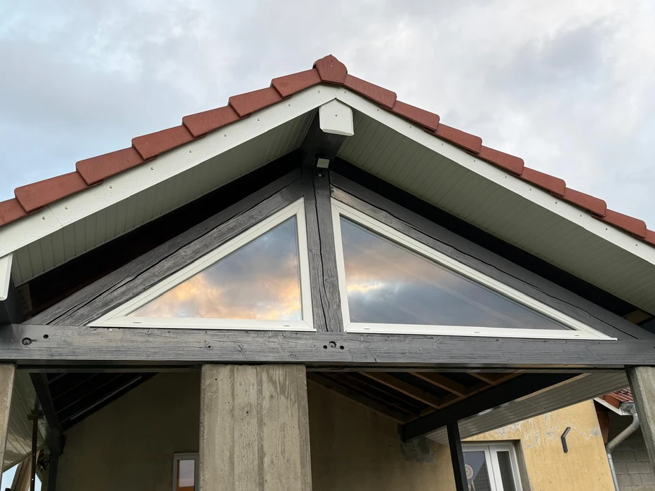 Façade de maison vue en contre-plongée, pignon triangulaire avec deux fenêtres triangulaires en PVC blanc à vitrage réfléchissant