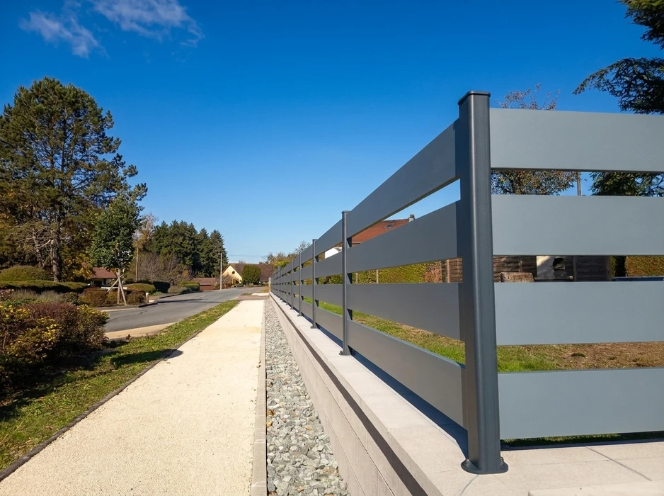 Clôture aluminium laqué gris anthracite à lames horizontales, installée en limite de propriété le long d'une allée gravillonnée