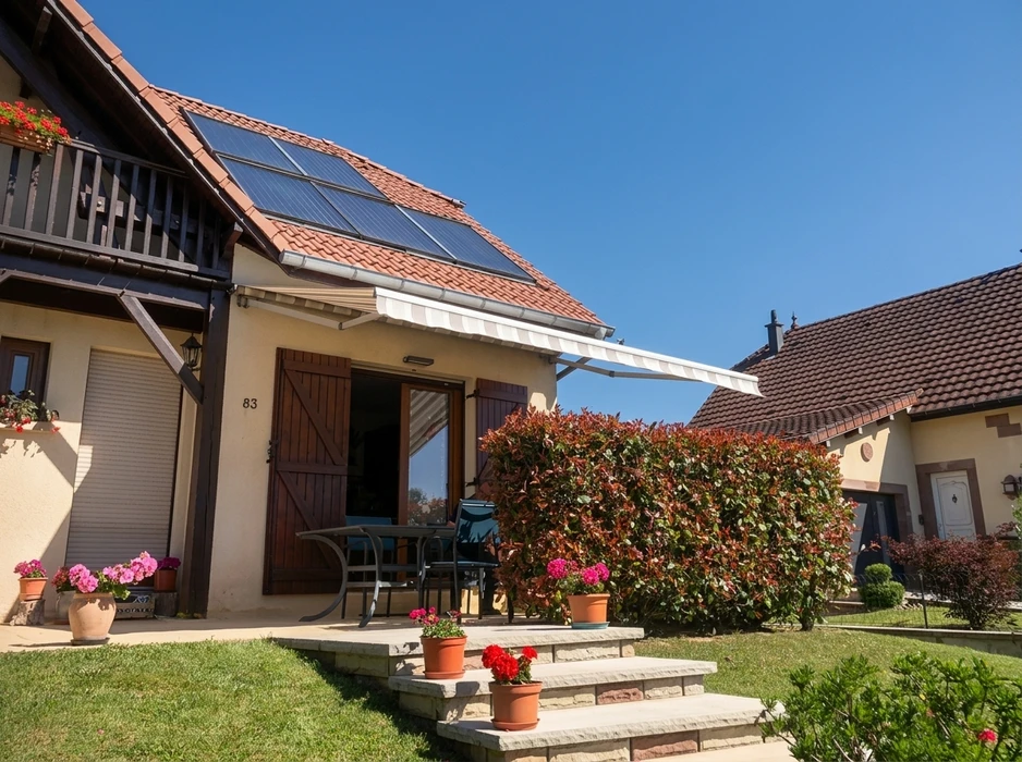 Maison individuelle de style alsacien, façade crépi beige, toiture en tuiles terre cuite équipée de **capteurs solaires thermiques** (3 panneaux plats)
