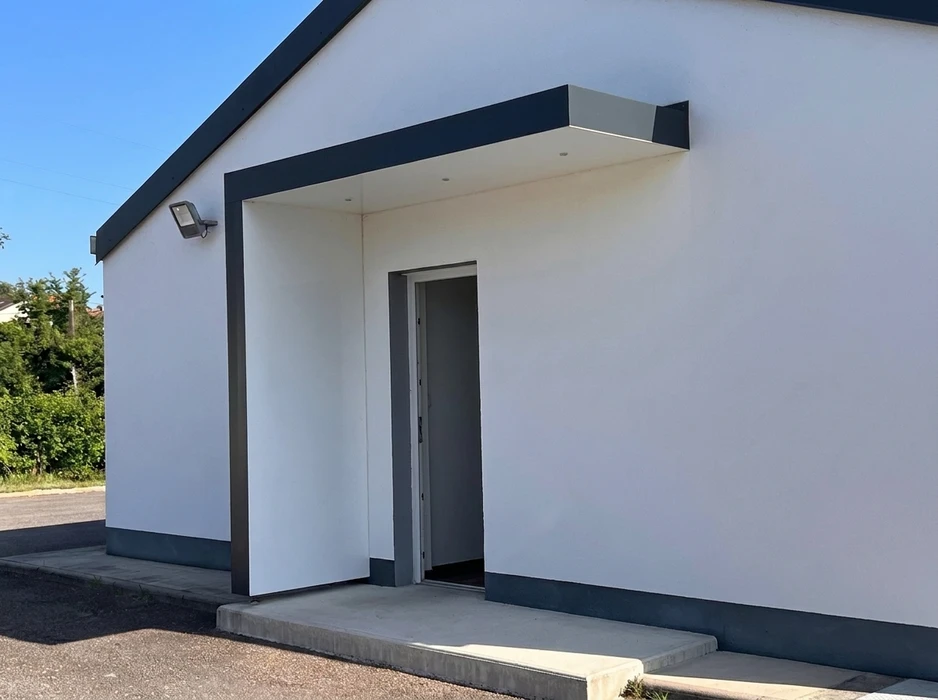 Porte d'entrée moderne en aluminium anthracite, posée dans une arche en pierre calcaire blanche sur façade enduite couleur saumon