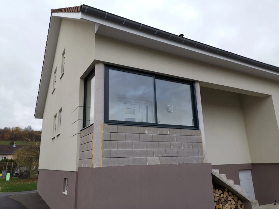 Terrasse extérieure d'une maison individuelle de plain-pied, équipée d'une pergola bioclimatique aluminium anthracite à lames orientables blanches, fixée en façade