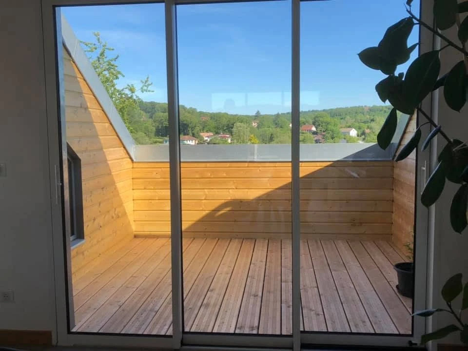 Terrasse extérieure d'une maison individuelle de plain-pied, équipée d'une pergola bioclimatique aluminium anthracite à lames orientables blanches, fixée en façade