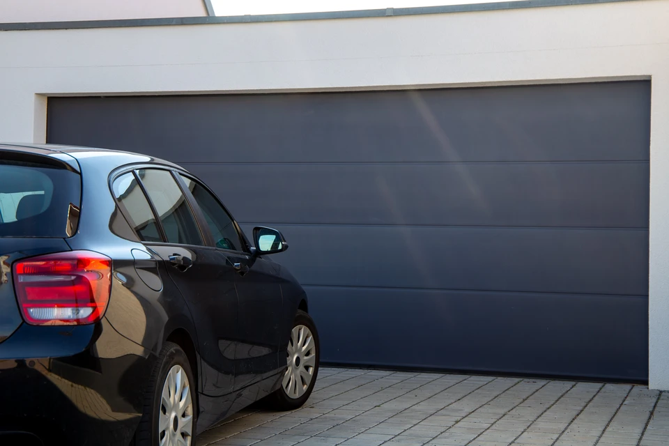 Extérieur résidentiel moderne avec porte de garage sectionnelle anthracite à panneaux horizontaux intégrée dans façade bicolore gris foncé et blanc