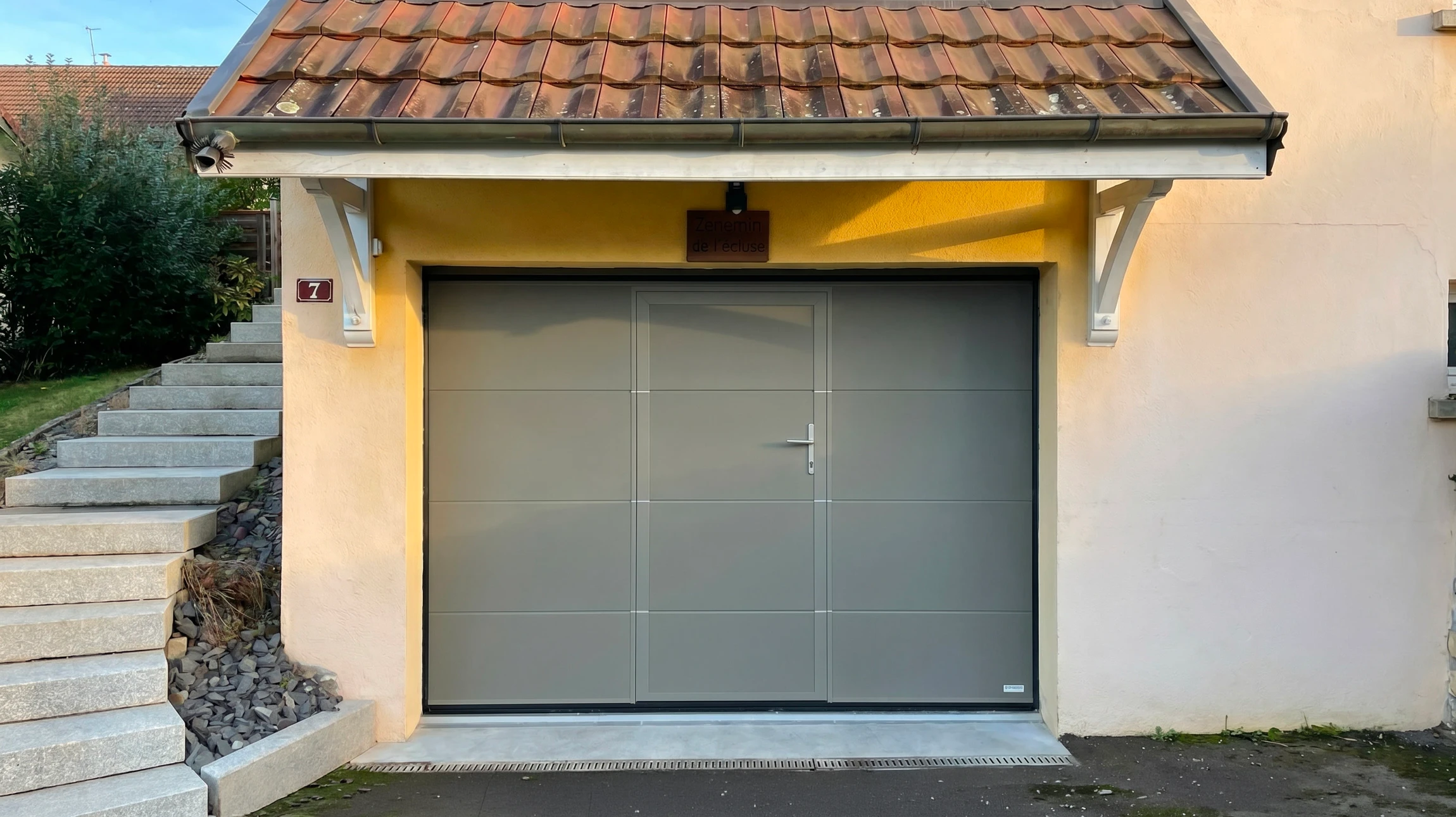 Deux techniciens en combinaisons de travail et casques orange installent une porte de garage sectionnelle blanche dans un garage résidentiel
