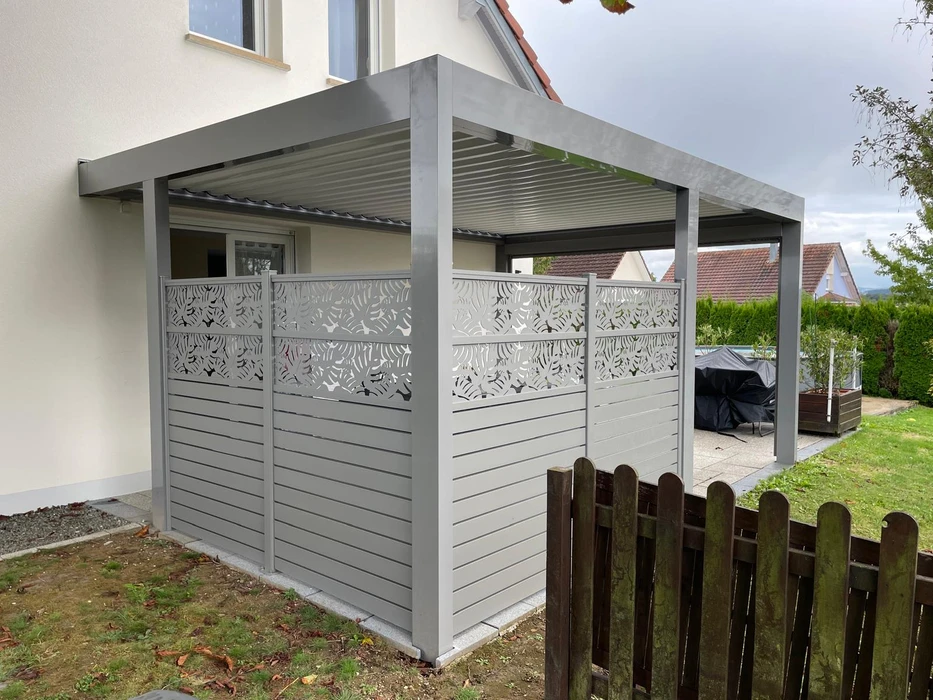 Terrasse extérieure avec pergola bioclimatique à lames orientables en aluminium anthracite, adossée à une maison contemporaine en crépi blanc