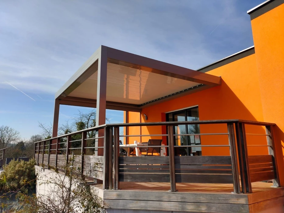 Terrasse moderne en dallage béton avec pergola bioclimatique aluminium anthracite à lames orientables, adossée à une maison contemporaine