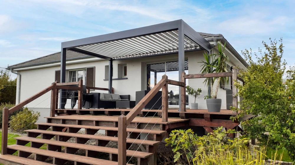 Terrasse moderne en dallage béton avec pergola bioclimatique aluminium anthracite à lames orientables, adossée à une maison contemporaine