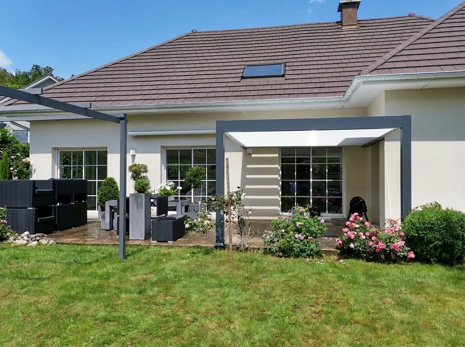 Terrasse moderne en dallage béton avec pergola bioclimatique aluminium anthracite à lames orientables, adossée à une maison contemporaine