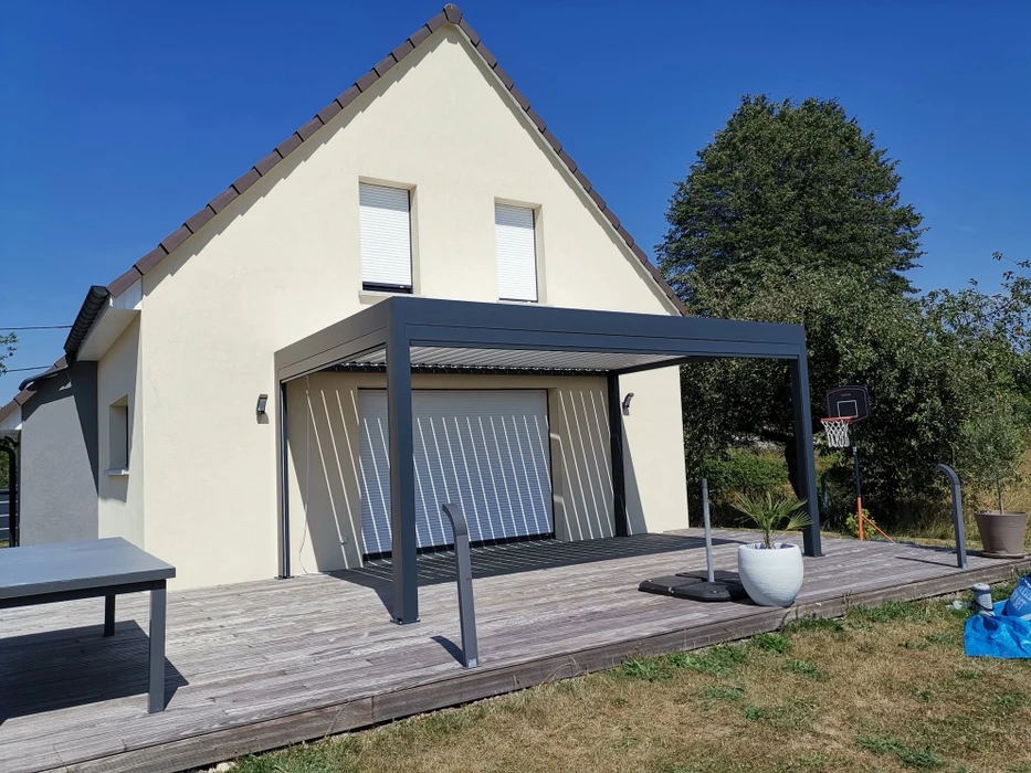 Terrasse extérieure d'une maison individuelle de plain-pied, équipée d'une pergola bioclimatique aluminium anthracite à lames orientables blanches, fixée en façade