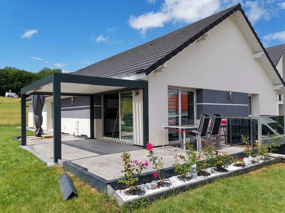 Pergola bioclimatique à lames orientables en aluminium anthracite, fixée en applique sur façade de maison individuelle en bardage clin beige