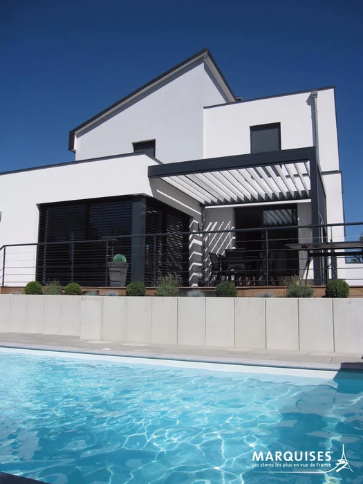 Terrasse extérieure couverte par une pergola bioclimatique à lames orientables en aluminium anodisé gris, fixée en applique murale
