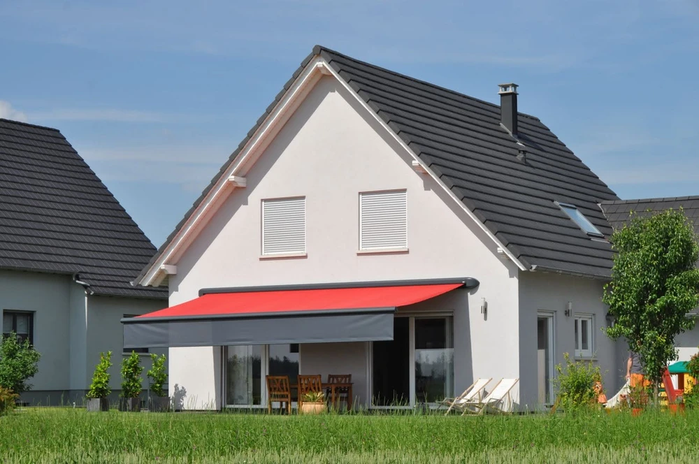 Un ouvrier portant une casquette noire et un polo bleu installe une moustiquaire sur une fenêtre à battants depuis l'intérieur d'un appartement en hauteur