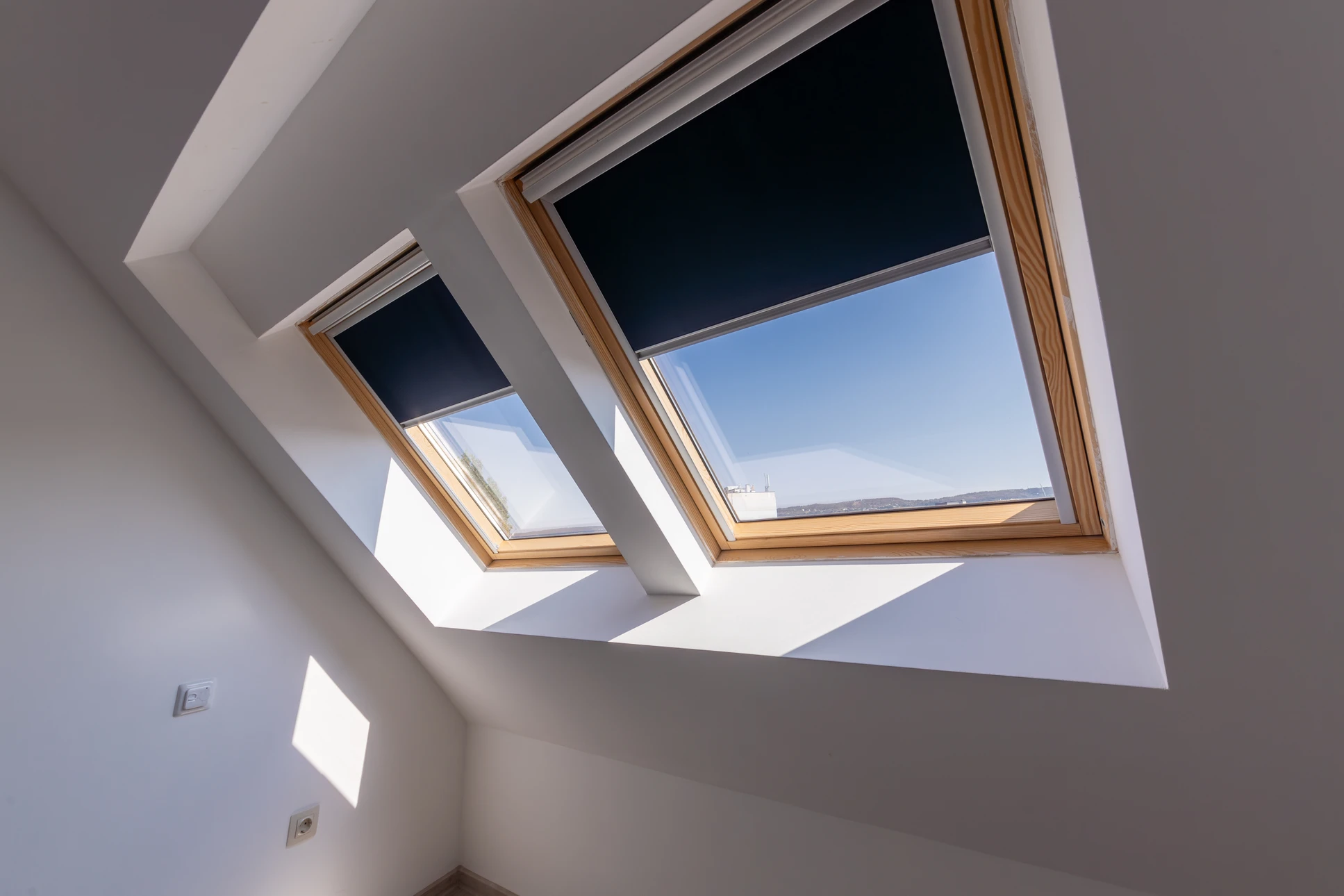 Photographie réaliste en haute résolution d'un intérieur de chambre ou pièce sous combles avec une grande fenêtre de toit Velux installée, laissant entrer la lumière naturelle abondante. La fenêtre de toit doit être clairement visible et bien mise en évidence. La pièce est moderne, bien aménagée avec mobilier, et la fenêtre offre une vue dégagée sur le ciel et possiblement le paysage extérieur. Le style doit être contemporain et accueillant, reflétant une habitation rénovée de qualité.